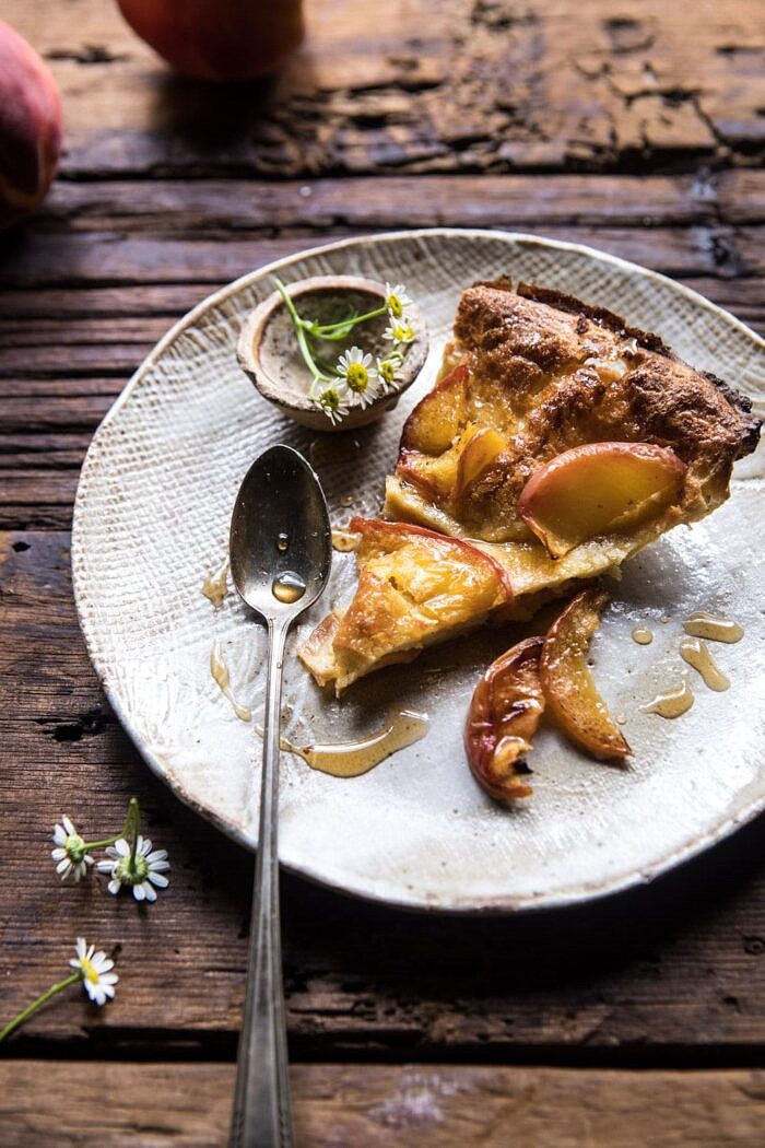Browned Butter Cinnamon Peach Dutch Baby on a plate with spoon and flowers