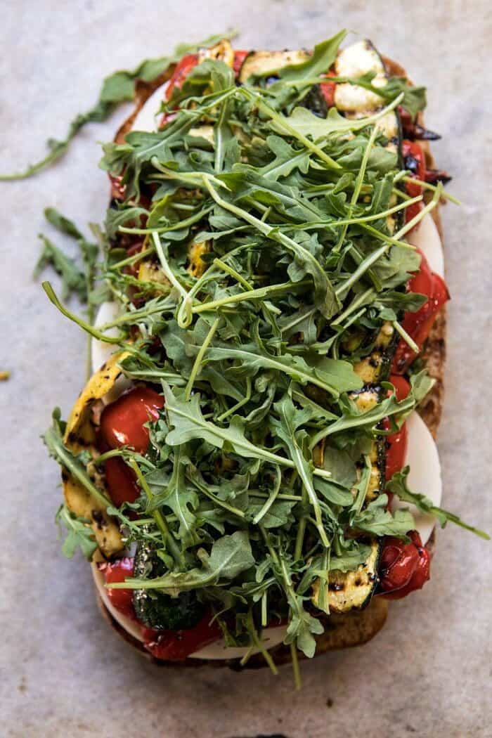 overhead photo of Marinated Veggie Cheese Sandwich with Sun-Dried Tomato Pesto and arugula on top