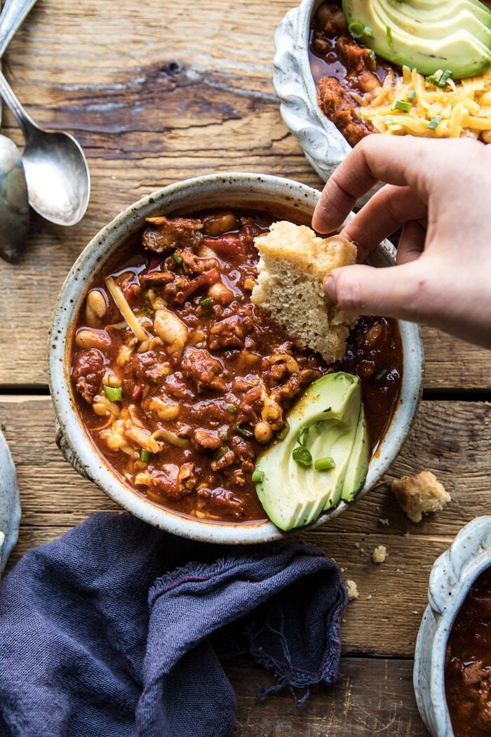 overhead photo of Healthy Slow Cooker Turkey and White Bean Chili with hand in photo dipping bread into chili bowl