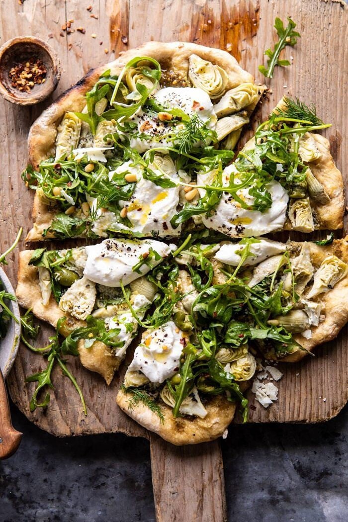 overhead photo of Artichoke Pesto and Burrata Pizza with Lemony Arugula with pieces cut