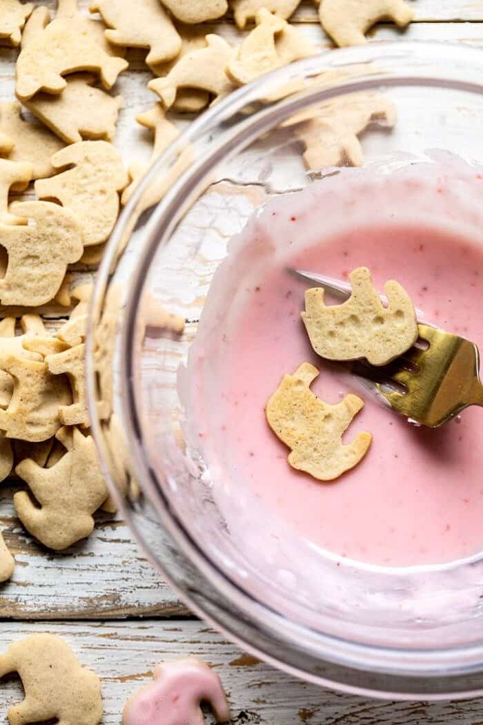 Homemade Animal Crackers being dipped in pink strawberry glaze 
