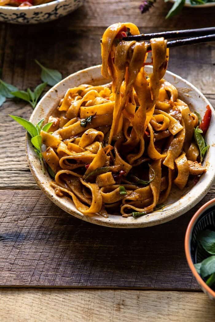 side angled photo of Better Than Takeout Thai Drunken Noodles with chopsticks pulling noodles out of the bowl to eat