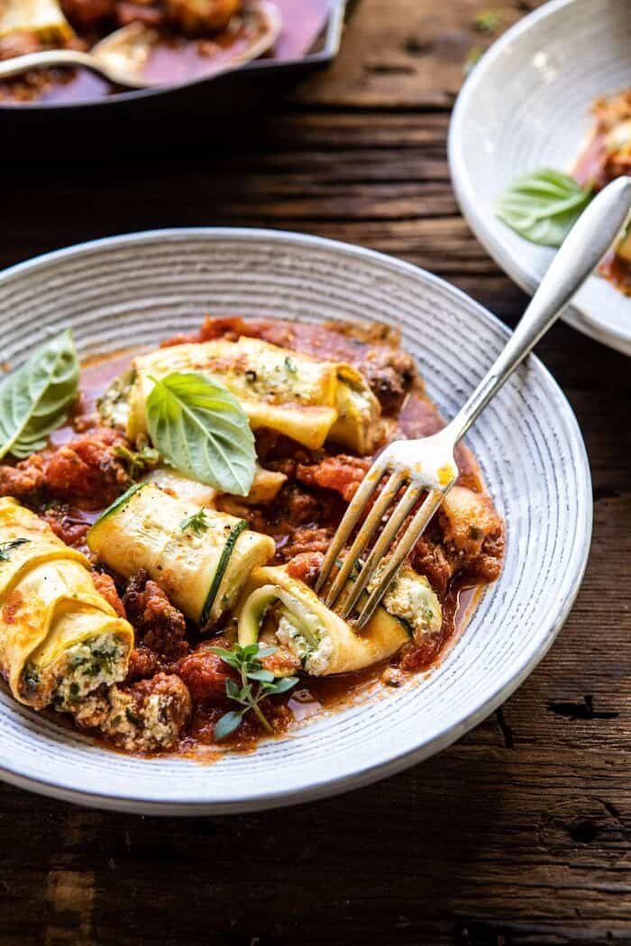 side angled photo of Spicy Pesto and Cheese Stuffed Zucchini Involtini on a plate with fork in a zucchini to reveal the cheese inside