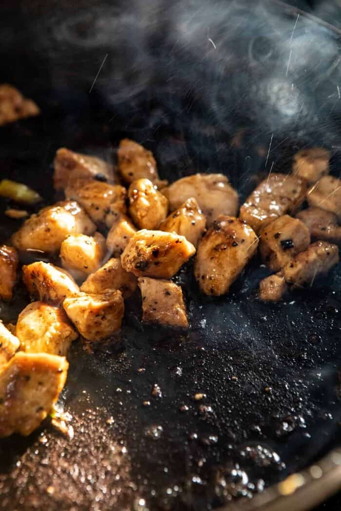 side angled prep photo of chicken cooking in skillet on stove