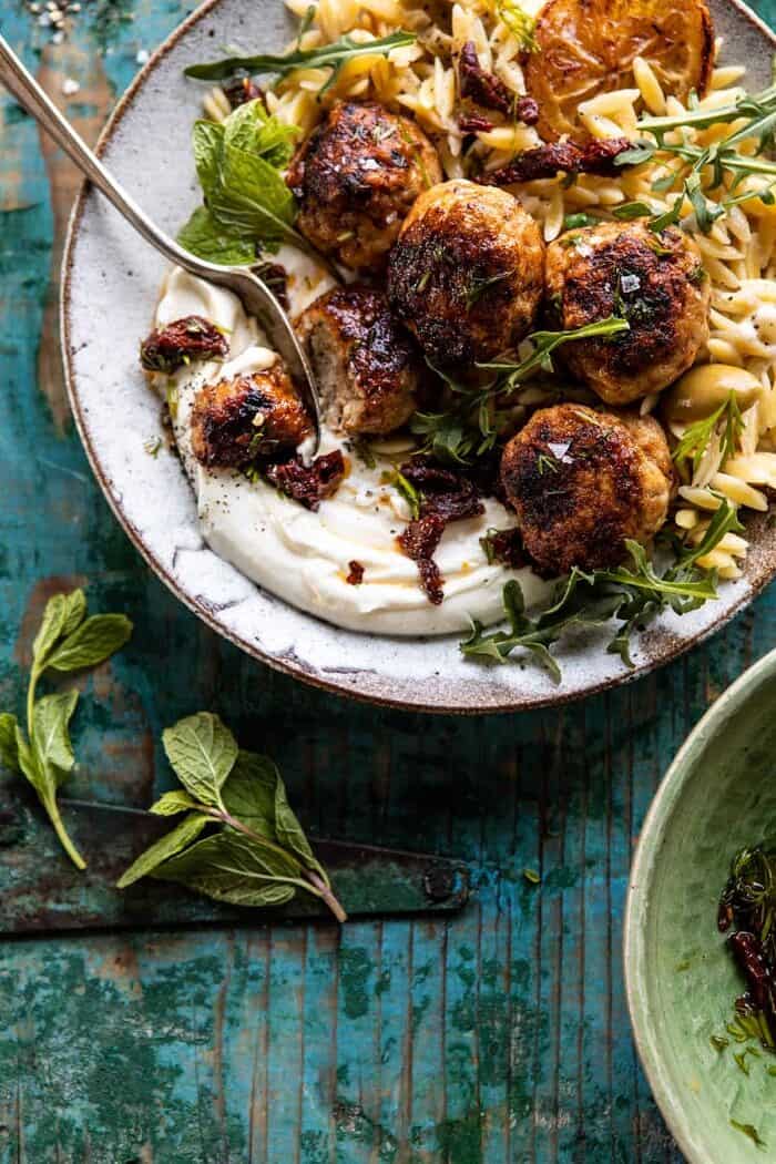 overhead photo of One Skillet Greek Meatballs and Lemon Butter Orzo and bite taken out of meatball