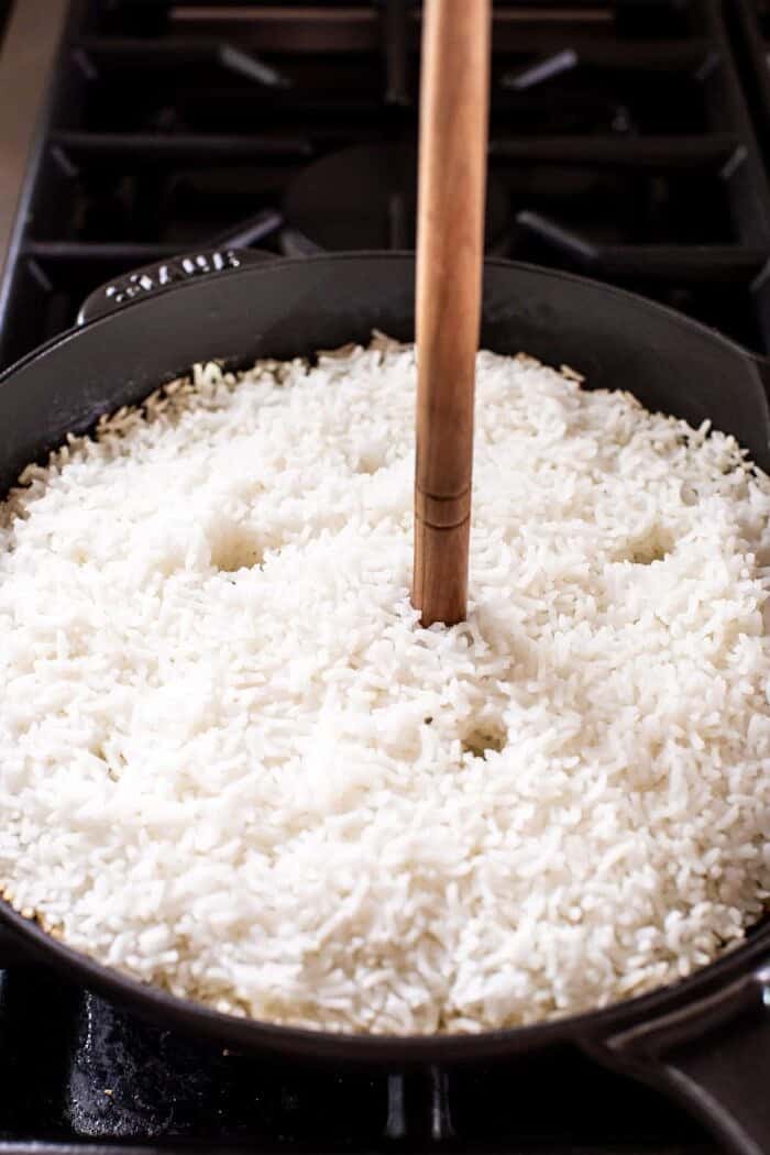 wooden spoon being inserted into rice to create holes