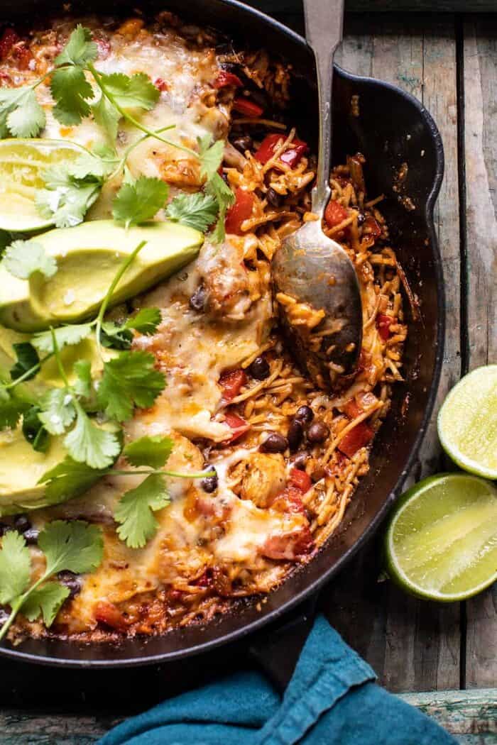 overhead close up photo of One Skillet Cheesy Cuban Chicken Rice Bake with spoon in skillet and portion of rice removed