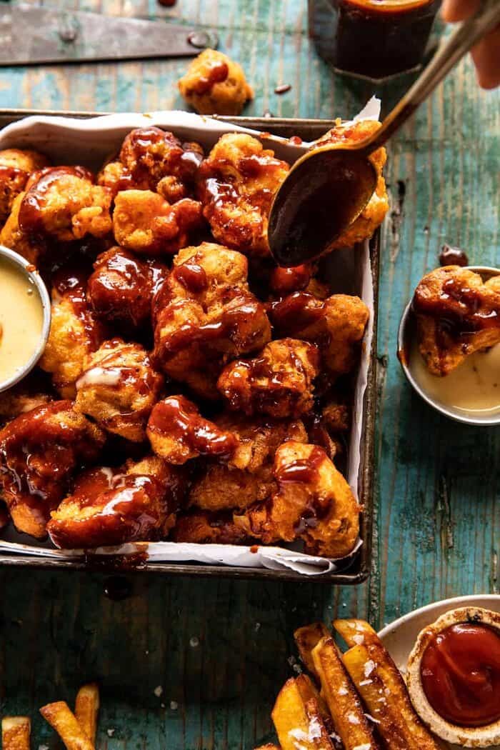 overhead photo of Crispy Beer Battered BBQ Cauliflower Nuggets being drizzled with BBQ sauce 