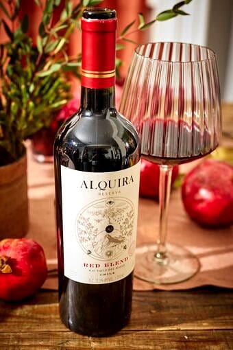 bottle of red wine next to a glss sitting on a wooden table